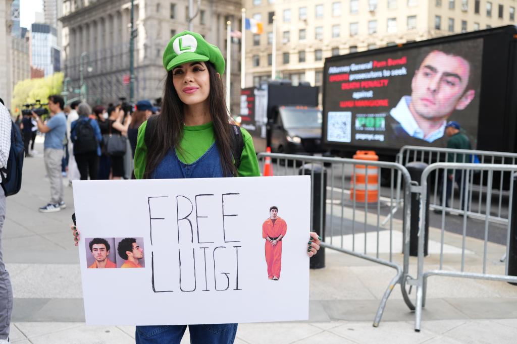 A woman in Luigi costume from Super Mario Brothers, holding a "Free Luigi" sign.
