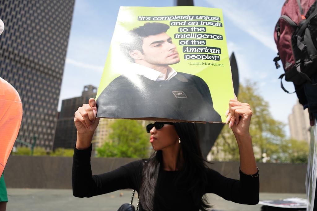 Woman holding up a sign with a photo of Luigi Mangione and the quote "It's completely unjust and an insult to the intelligence of American people."