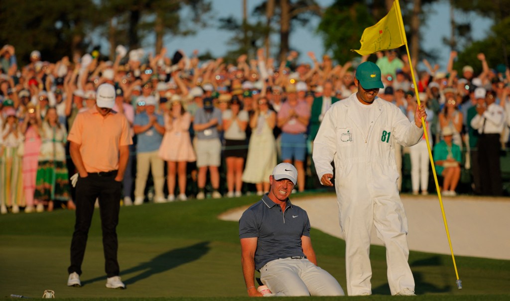 Rory McIlroy celebrates on the 18th green of the 1st play-off hole after winning The Masters and completing a career grand slam with his caddie Harry Diamond holding the pin and England's Justin Rose in the background on April 13, 2025. 