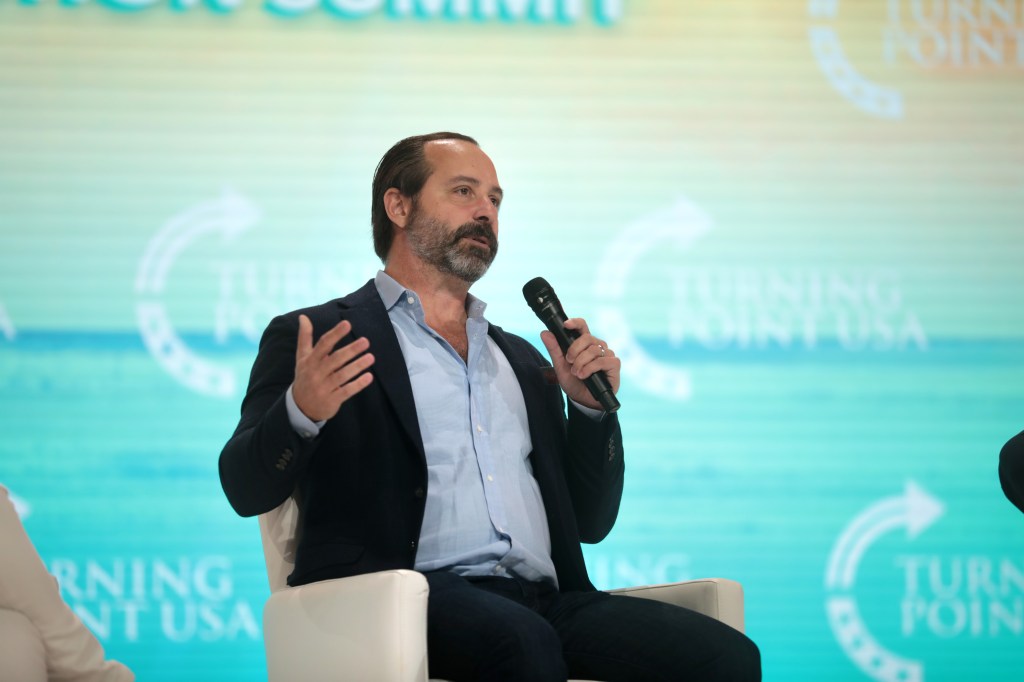 Chris Buskirk sitting in a chair holding a microphone, speaking to attendees at the 2021 Student Action Summit in Tampa, Florida
