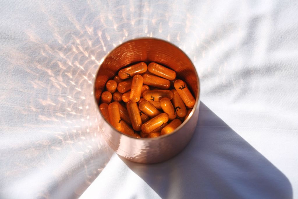 A copper jar with golden supplements inside.