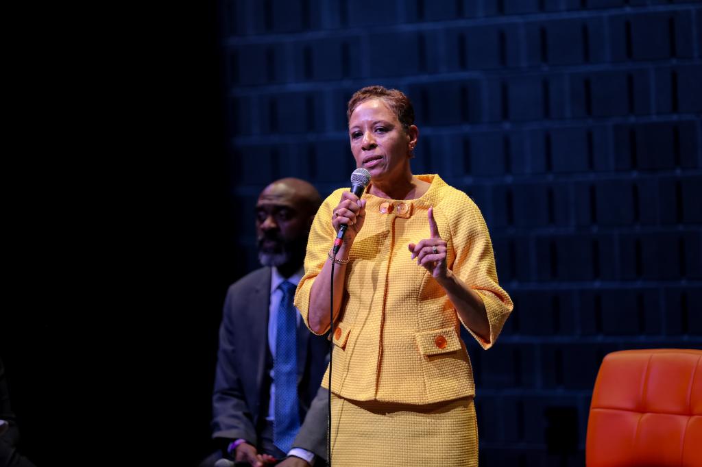Council speaker adrienne adams, holding a microphone and wearing a yellow suit