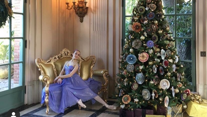 Anya Varfolomeev wearing purple dress and pointe shoes next to a Christmas tree