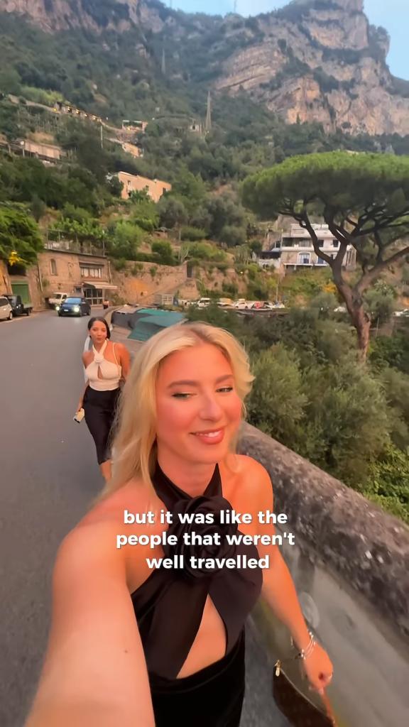 Blonde woman in a black dress taking a selfie video on a hillside road in Italy