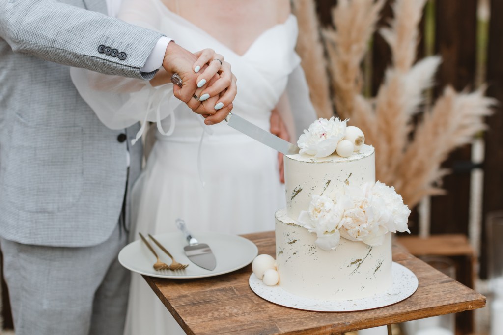 Bride and groom cutting their wedding cake decorated with delicate white flowers at an outdoor reception