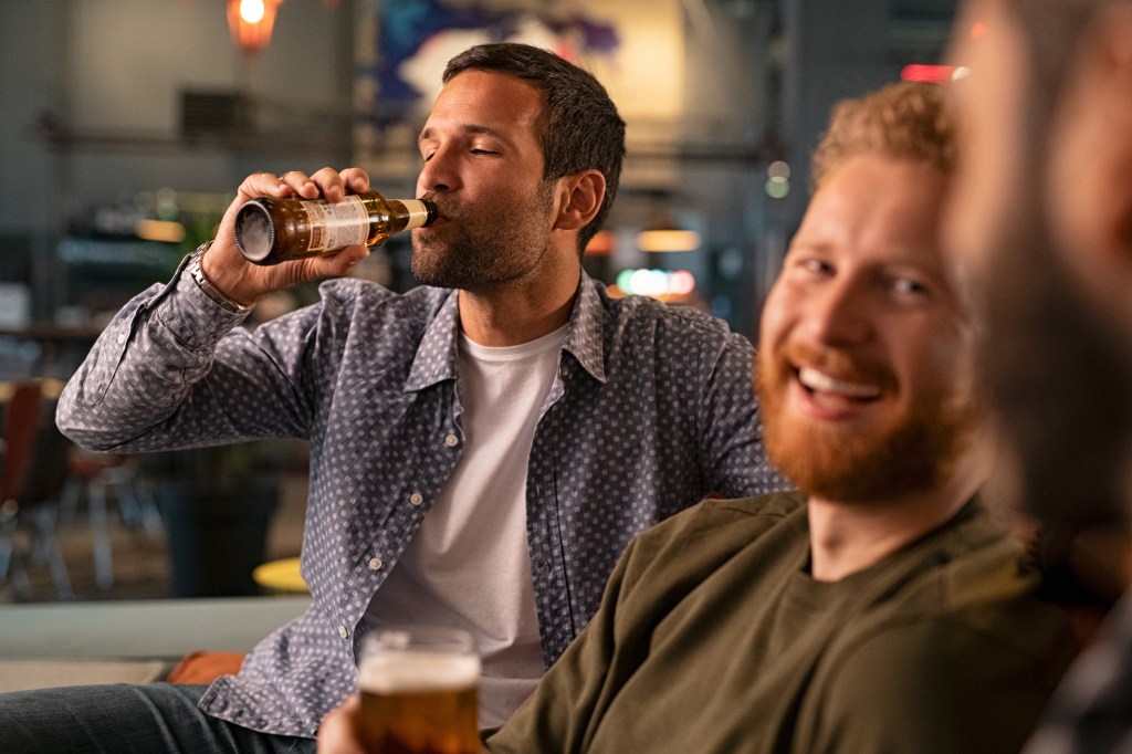 A man drinks a beer at a bar with friends. 