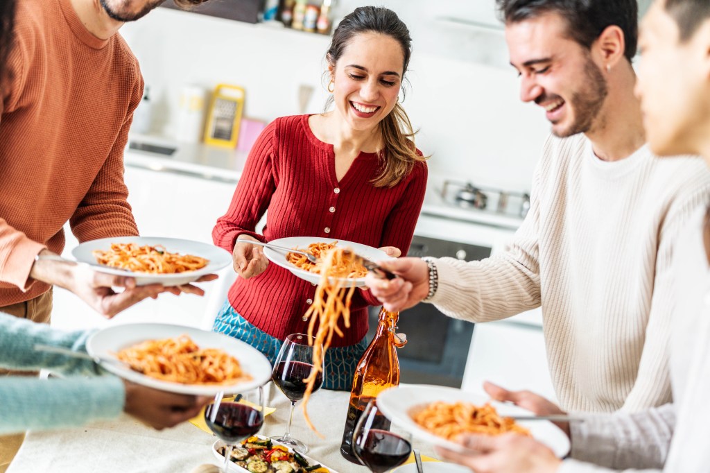 Happy group of friends eating pasta at home dinner party.