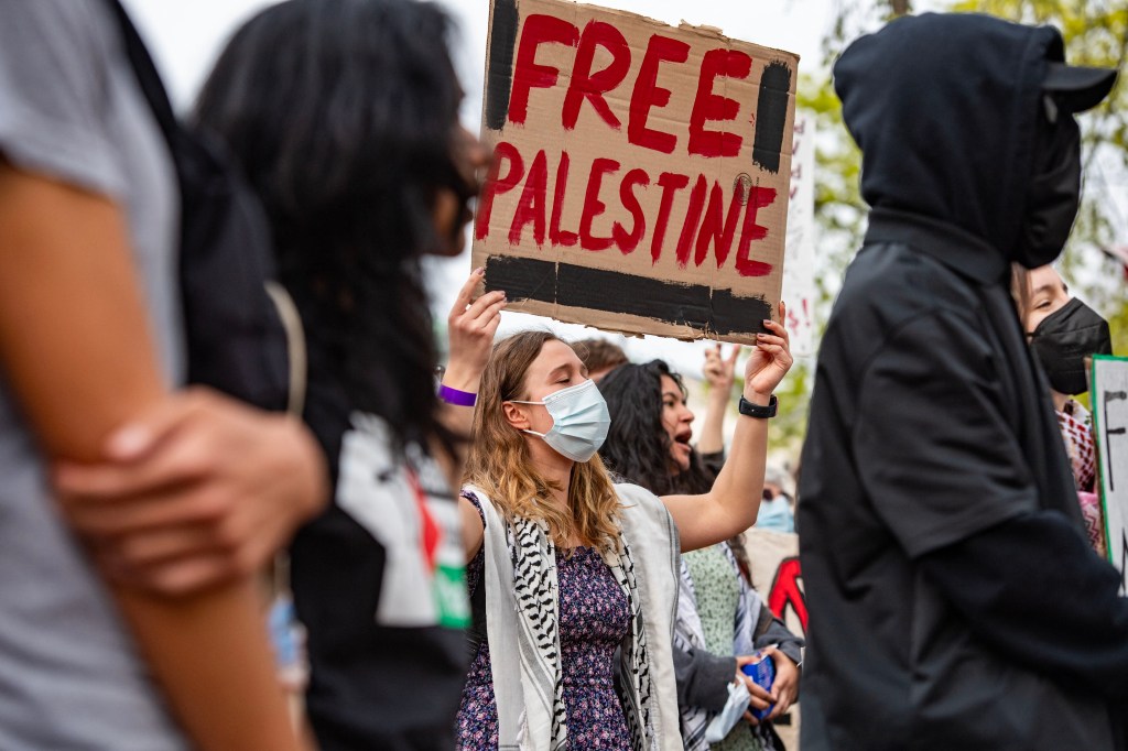 Demonstrators protesting Harvard's stance on the war in Gaza, showing support for the Palestinian people outside Harvard University, with a woman prominently holding a sign