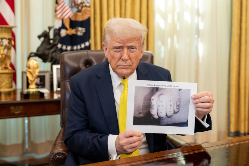 President Donald Trump holds up an inmage of Kilmar Abrego Garcia's knuckle tattoos in the Oval Office on April 18, 2025.