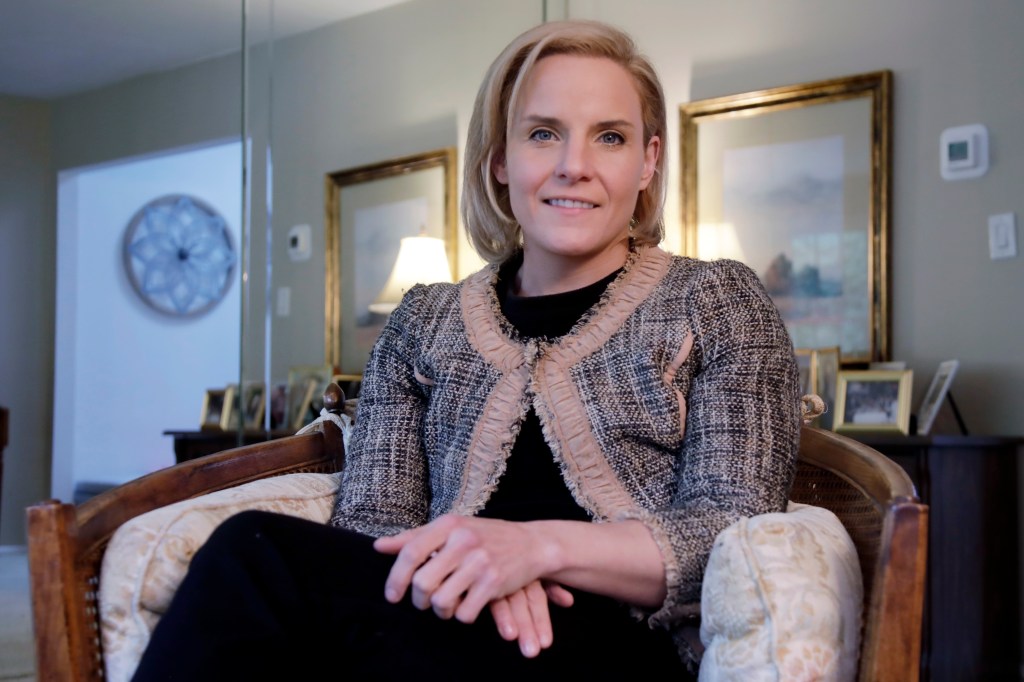 portrait of amanda reynolds, sitting in a white chair with her legs crossed and her hands on her lap