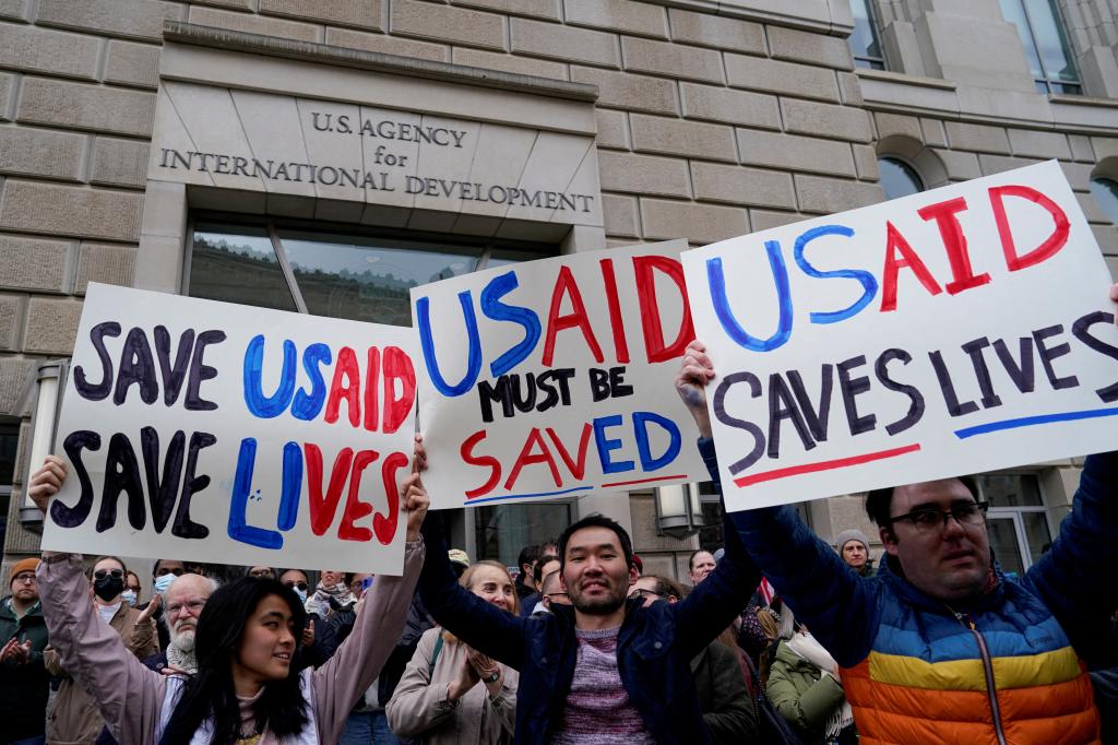 A group of people holding placards outside the closed USAID building in Washington, D.C. advising employees to work remotely