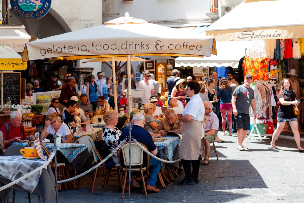A group of people sitting at tables outside a restaurant in Piazza Duomo, Amalfi, Costiera Amalfitana, Italy