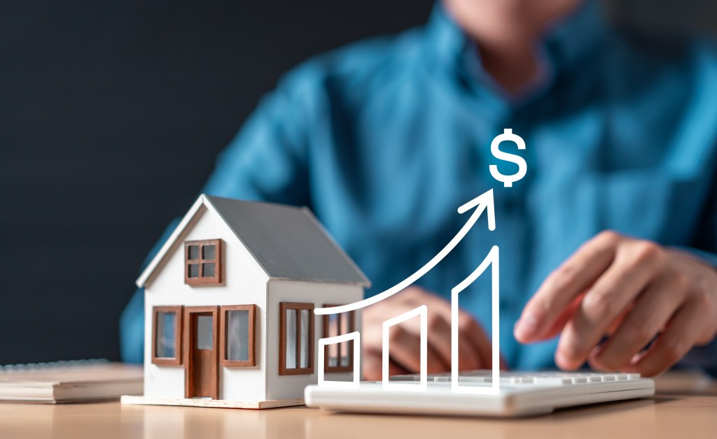 A person is typing on a keyboard in front of a house with a dollar sign on it and a chart.