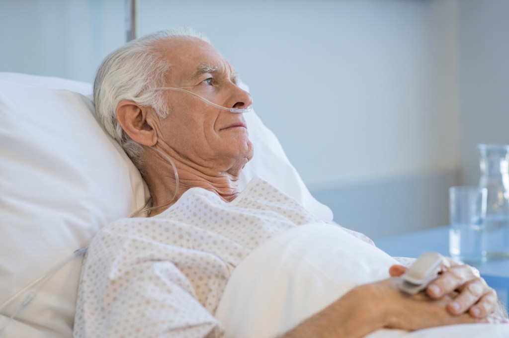 A senior man lays in a hospital bed. 