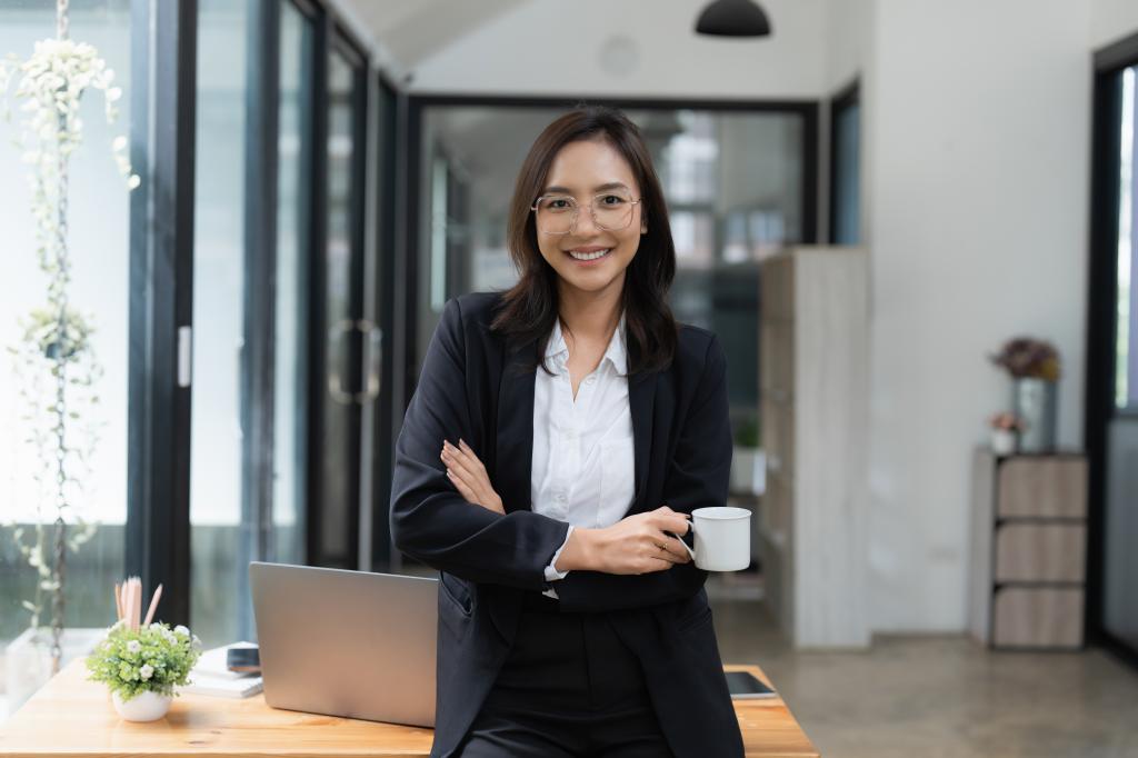 Smart Asian business woman in a suit, smiling and holding a cup in an office space