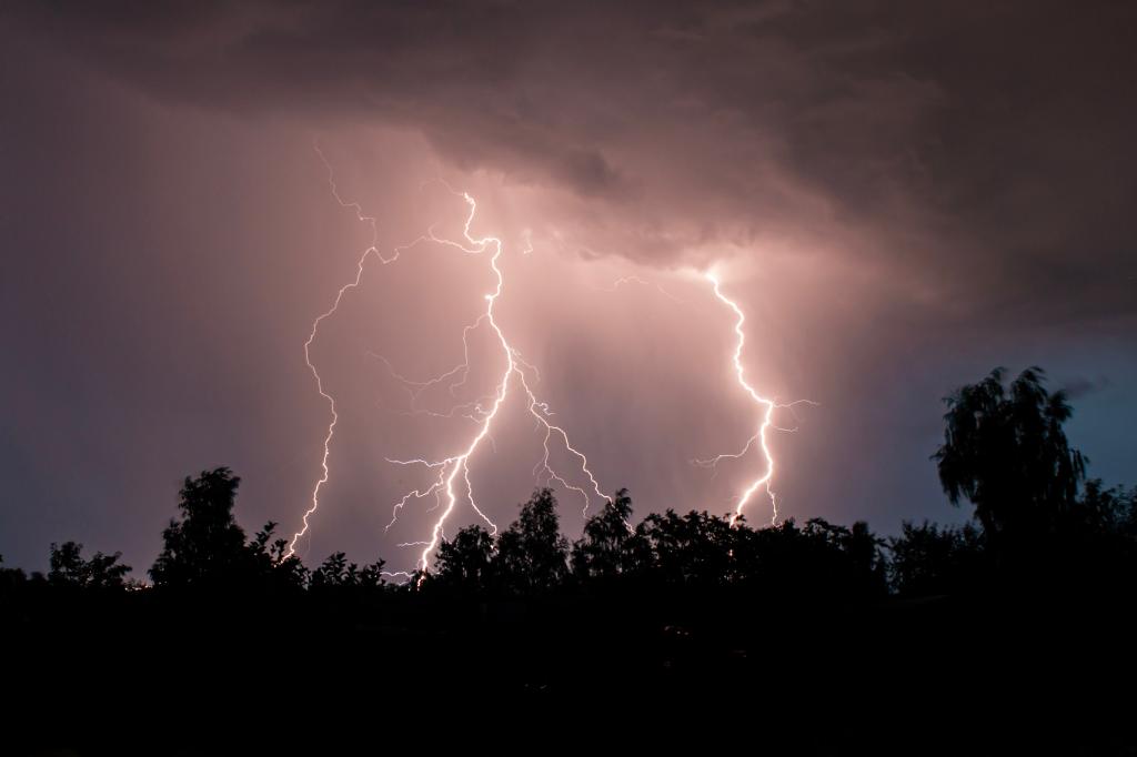 STOCK beautiful lightning during a thunderstorm at night in a forest that caused a fire, against a dark sky with rain