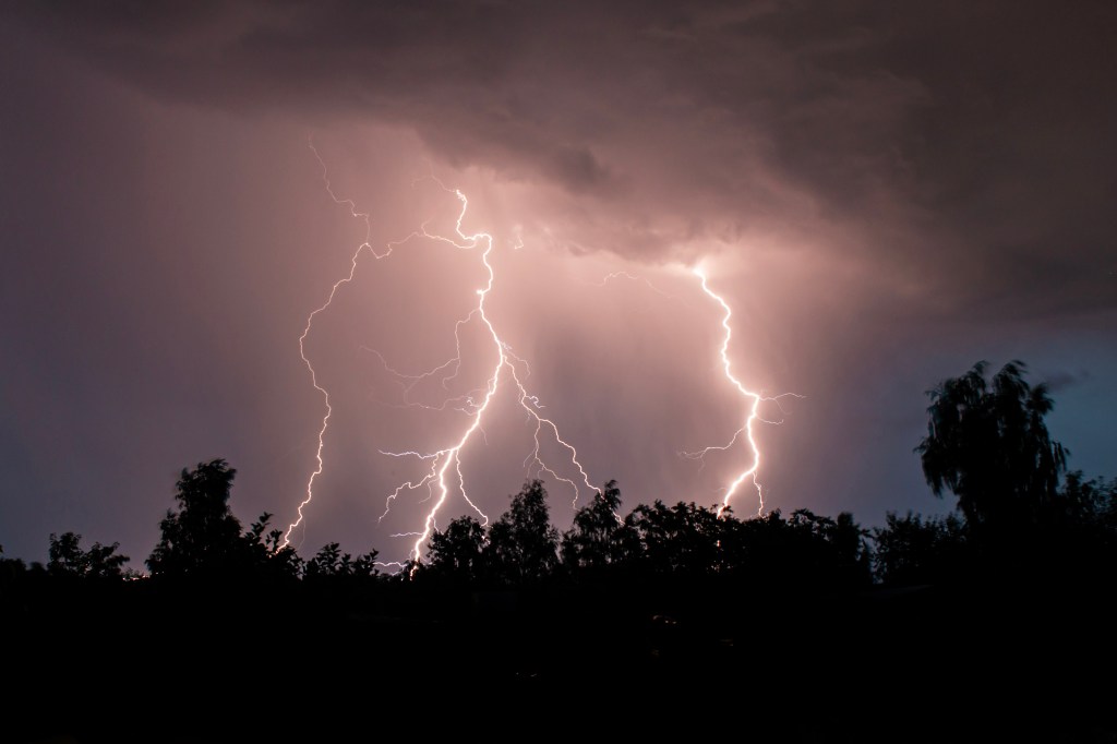 STOCK beautiful lightning during a thunderstorm at night in a forest that caused a fire, against a dark sky with rain