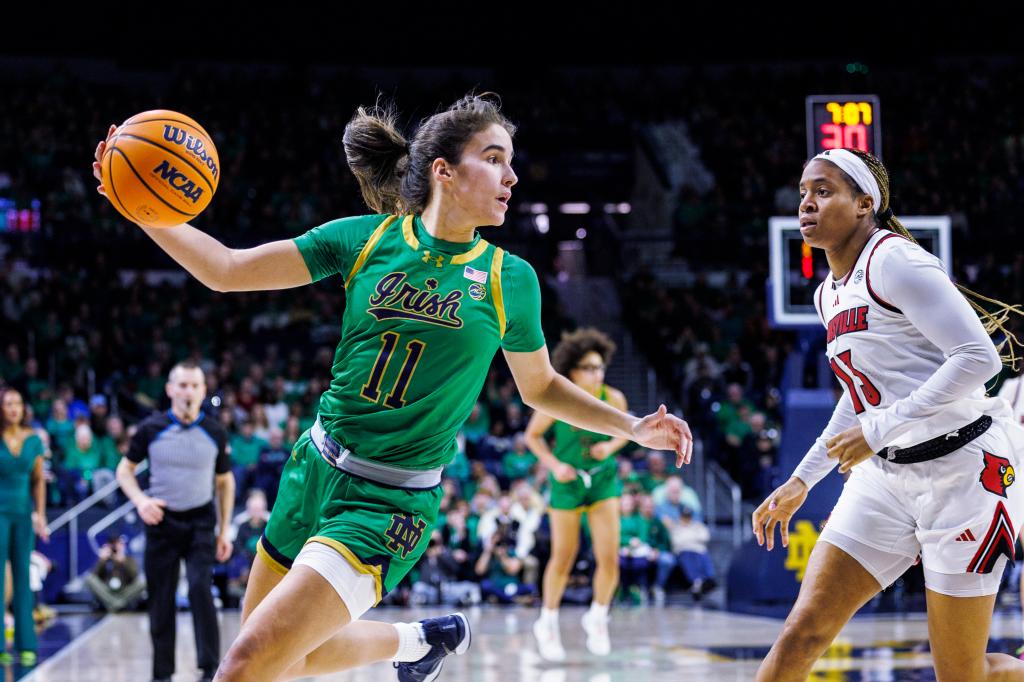 Notre Dame guard Sonia Citron in green uniform, tracking down the basketball with Louisville guard Merissah Russell defending, during a 2025 NCAA college basketball game