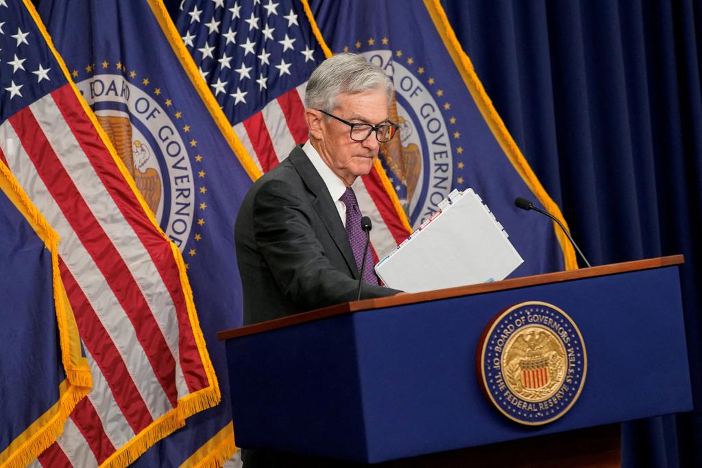 U.S. Federal Reserve Chair Jerome Powell standing at a podium with a microphone and flags, holding a press conference in Washington, D.C.