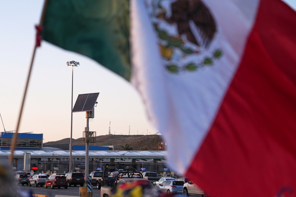 A Mexican flag waves as people and vehicles wait to cross the border into the US on March 18, 2025.
