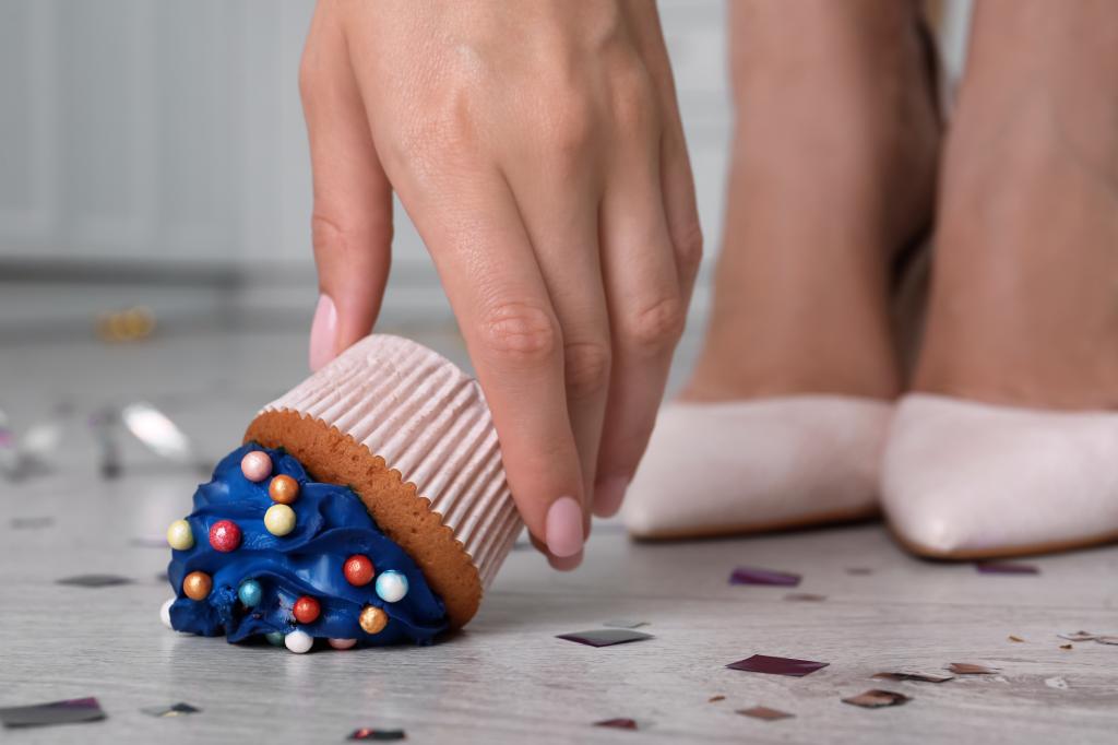 A woman picking up a dropped cupcake.
