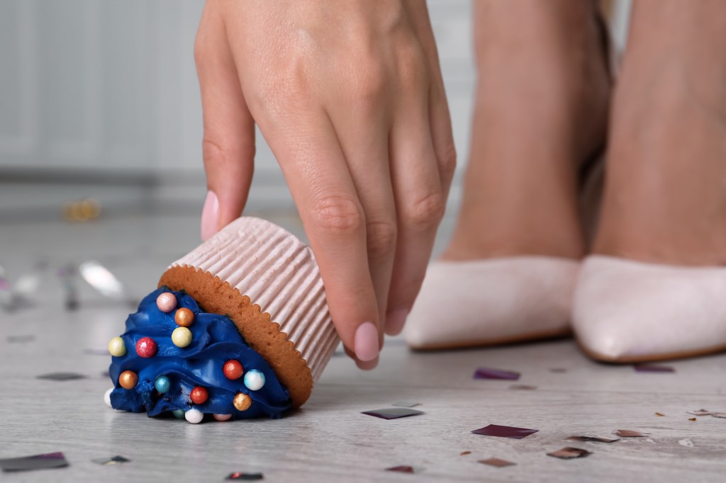 A woman picking up a dropped cupcake.