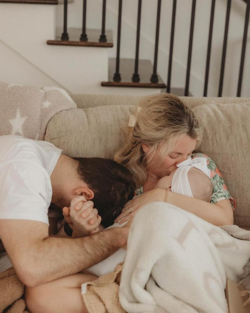 A man and woman kissing their 9-month-old baby on a couch