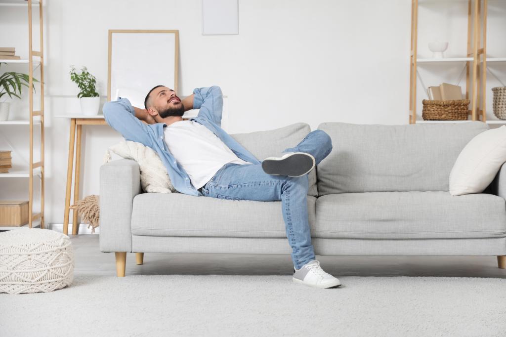 A young man lying on a couch with his hands behind his head, resting on his day off at home