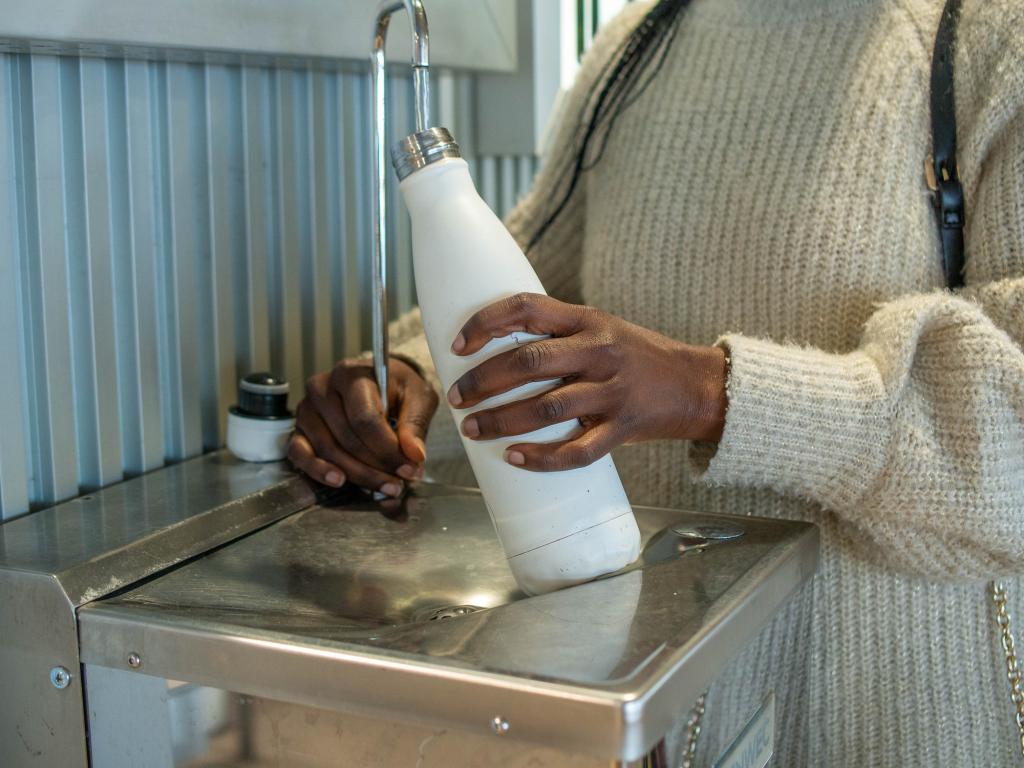 Bring a bottle from home and fill up on the free water. Here, a woman fills up her reusable bottle at an airport water fountain.