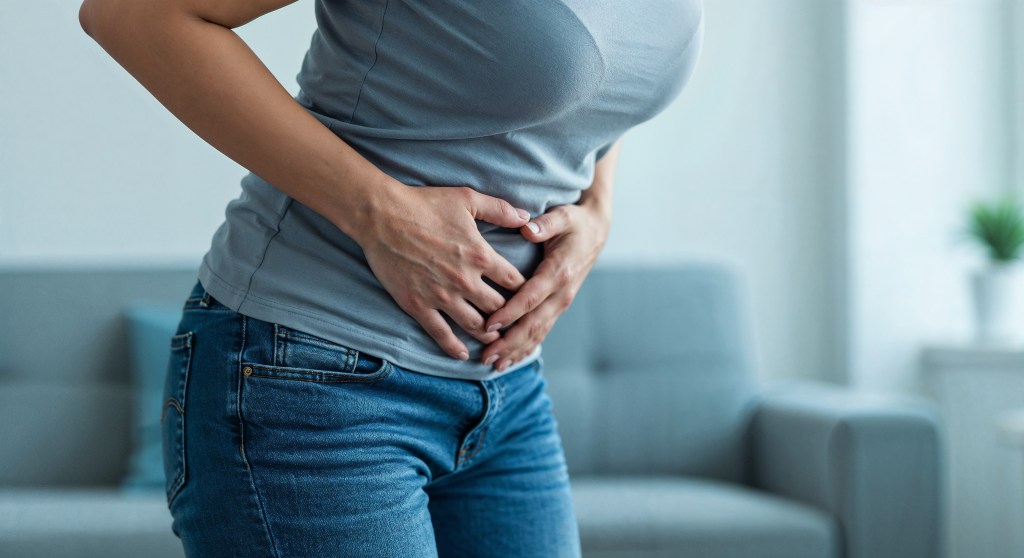 Woman at home clutching abdomen, experiencing abdominal cramps, depicting healthcare and digestive issues concepts