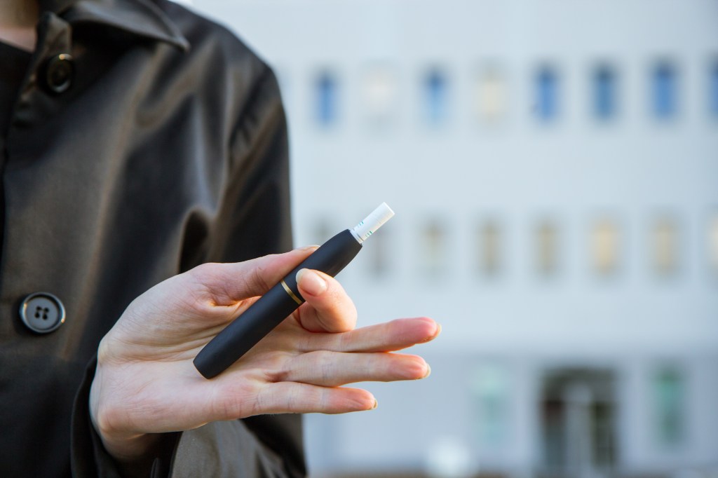 A woman holds out a heated tobacco product. 