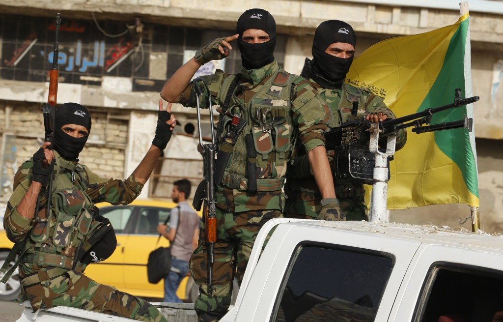 Hezbollah terrorists stand with weapons in back of white pick-up truck in Iraq.