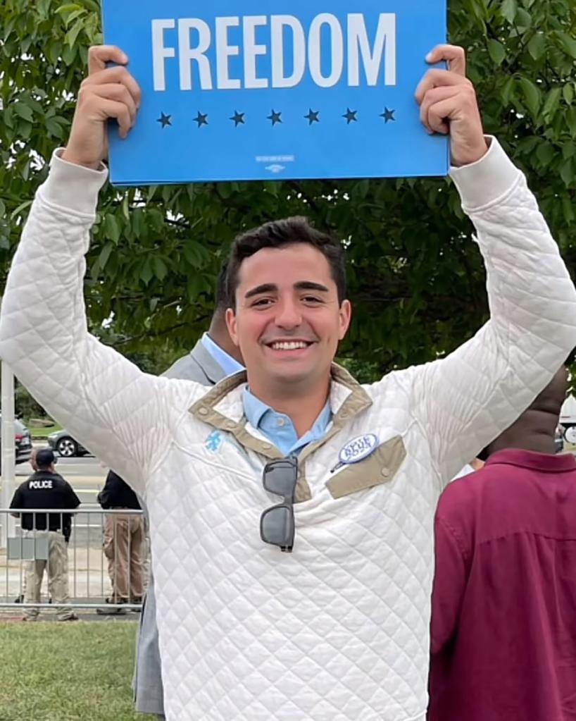 Petros Krommidas in an undated photo smiling and holding up a sign that says "freedom"
