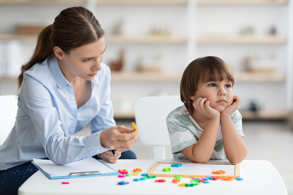Sad little boy ignoring his speech therapist and colorful letters in an office setting