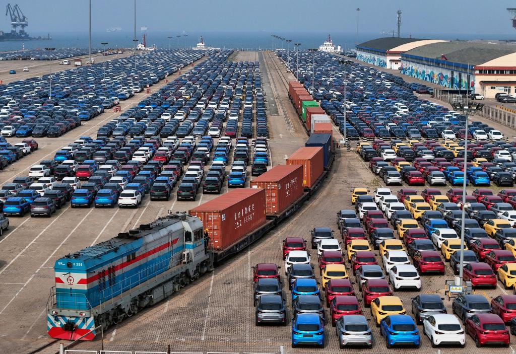 Cargo train passing by new cars ready for shipment at a port in Yantai, Shandong Province, China, symbolizing the US-China trade deal resolution