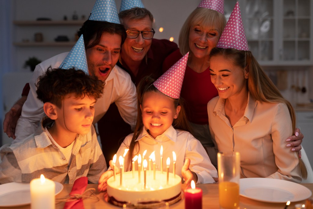 Little girl receiving a birthday cake with lit candles, celebrating with her extended family at home.