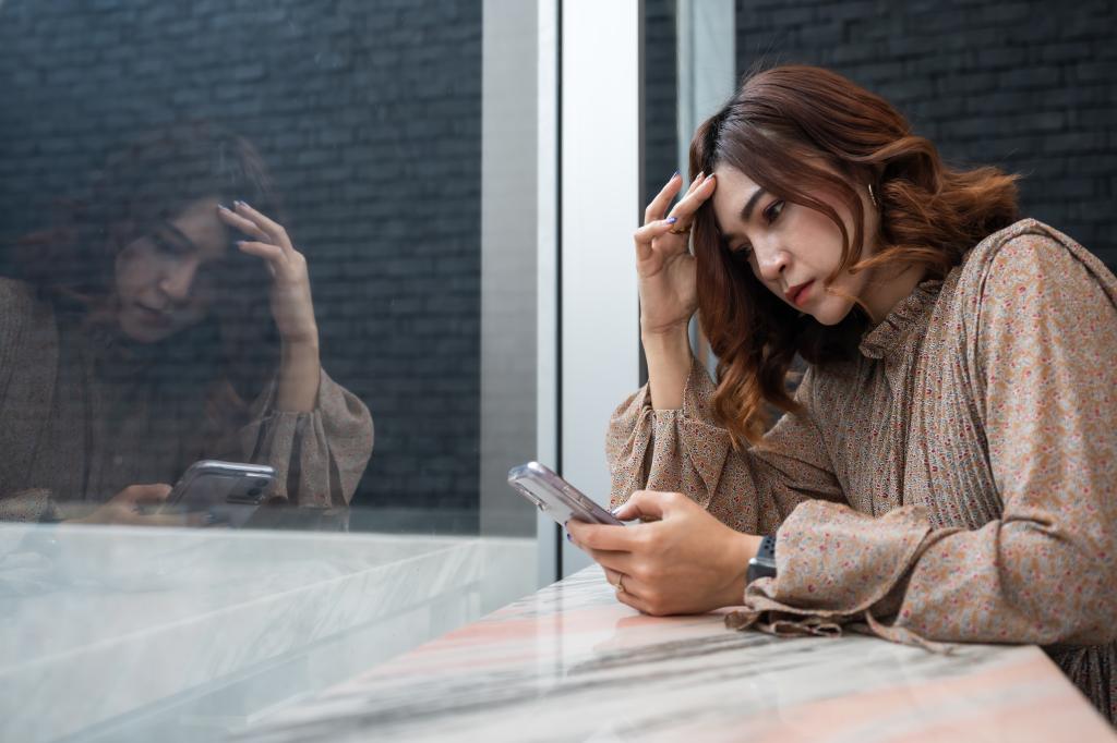 Depressed young woman looking at her smartphone and having a headache, feeling sad and worried about a problem