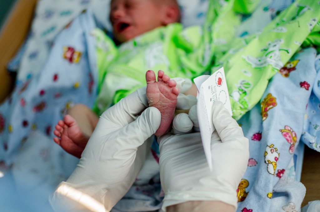 doctor takes blood sample from crying newborn 