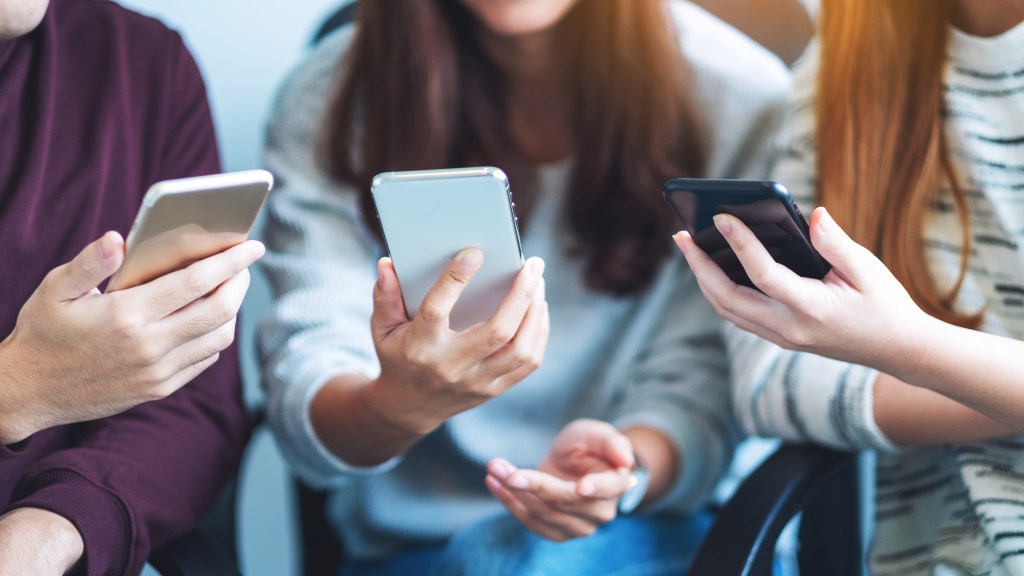 Group of young people using and looking at mobile phone while sitting together.