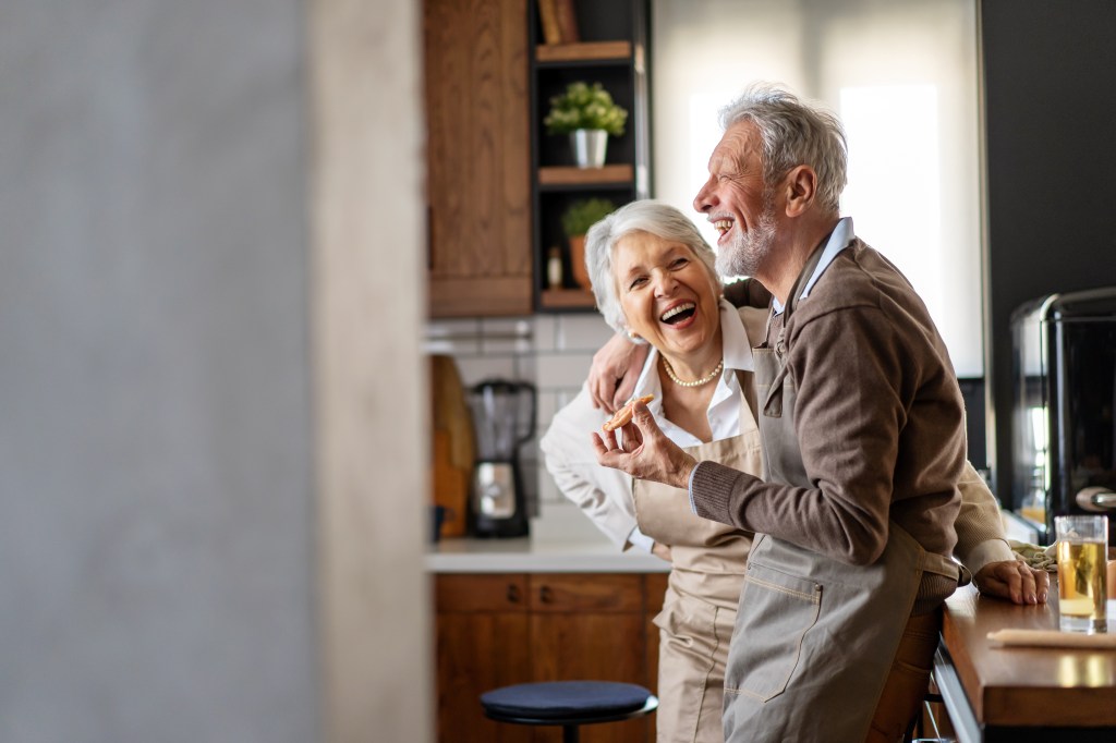 A happy elderly couple laughs in the kitchen. 
