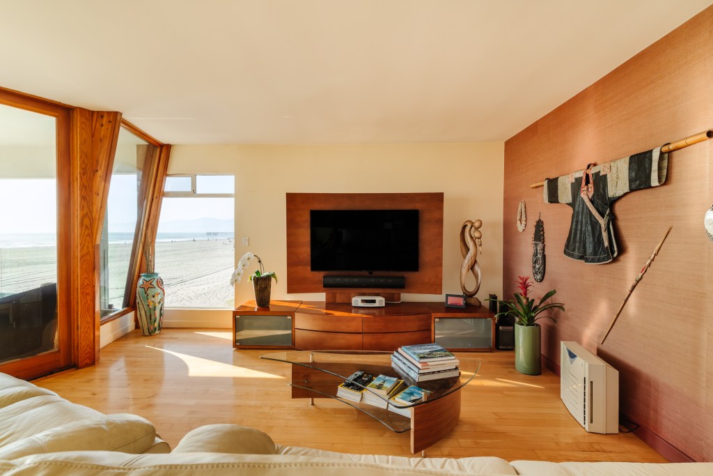 The space features a sunken living room, mirrored fixtures, wood-framed windows, and a glass balcony with panoramic ocean views. 