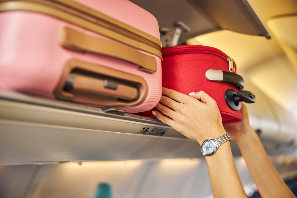 Hands placing carry-on luggage in overhead bin on airplane.